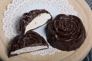 A chocolate marshmallow made in the shape of a rose lies on a white napkin. One marshmallow is cut in half, a slice is visible.