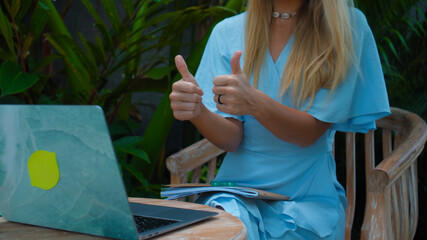 young girl sitting at a wooden table and working behind a laptop in a green garden
