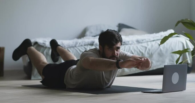 Young man doing boat exercise, watching example on laptop