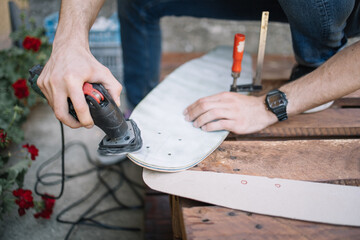 Close-up view of hands polishing wooden deck for skateboard. Cropped man using sander and polishing...