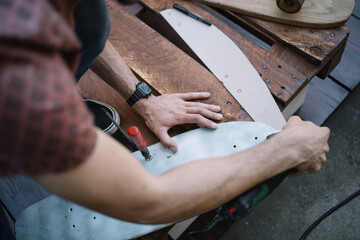 Top view of male hands polishing wooden board. Man's hands using sander and polishing wooden skateboard deck outdoor.