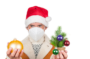 Man in Santa Claus hat and medical mask with christmas ball and fir tree on white background
