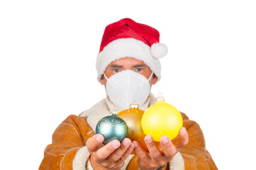 Man in Santa Claus hat and medical mask with christmas ball on white background. Front focus