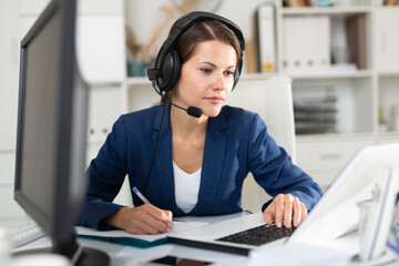 Portrait of positive woman call center operator receiving calls and using laptop in office