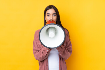 Young brunette woman over isolated yellow background shouting through a megaphone