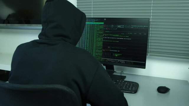 masked hacker using computer to hack data organizing massive data breach attacks on corporate servers located in a secret underground place wearing a black hoodie black cap and a scarf hidde identity