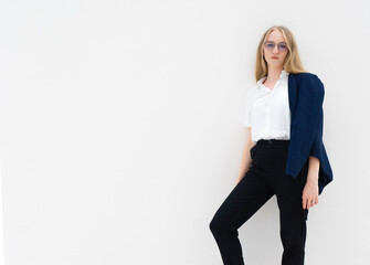 Fototapeta premium A young caucasian blonde business woman in glasses is standing in front of a white wall and looking to the camera. Concept of successful young women. Lifestyle concept. Copy space. Space for text.