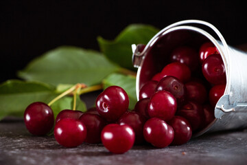 Ripe cherries scattered from an iron bucket on a dark table. Still life in a low key.