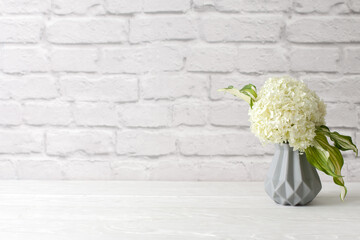 Green hydrangea in a gray vase in the Nordic style stands on a white wooden table. Background old brick. Bundle, copy space.