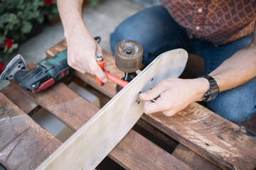 Close-up view of male hands screwing bolts to skateboard. Cropped man adding skateboard parts to deck in backyard.