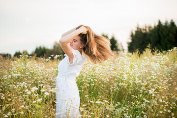 Obraz premium Happy girl on the camomile field, summer sunset. in a white dress. running and spinning, the wind in my hair, life style. freedom concept and hot summer