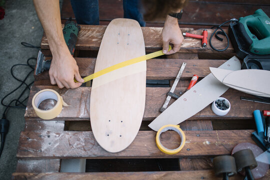 Man's hands sticking paper tape to wooden board. Wooden board with paper tape on table with power sander and set for making skateboard.