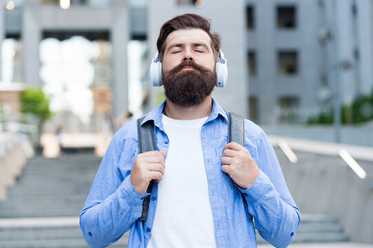 Modern life. Man with headphones walking city center. Listening music. Handsome hipster with backpack walking street. Good sound. Daily route to work. Walking through empty streets. Alone with music