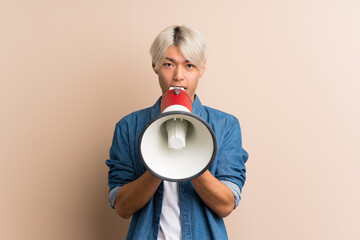 Young asian man over isolated background shouting through a megaphone