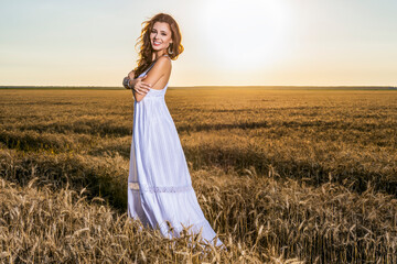 Fototapeta na wymiar A beautiful woman in a white dress in a wheat field at sunset.