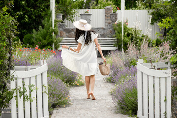 Fototapety  Dziewczyna z torebką w kapeluszu i sukience w lawendowym ogrodzie. letnia dziewczyna w prowansalskim stylu