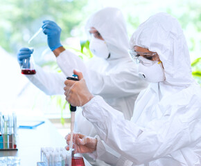 Scientists in protection suits and masks working in research lab using laboratory equipment: microscopes, test tubes.