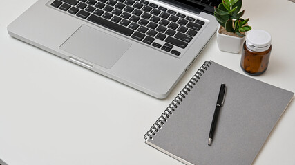 Cropped shot view of modern home office workspace with laptop, notebook and earphones on white table. Top view