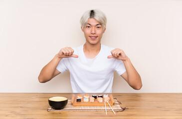 Young asian man with sushi in a table proud and self-satisfied