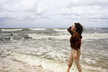 young woman walking on the beach and watching tide, windy day, wind in her hair, oceanic waves