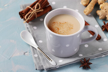 Traditional indian masala tea with spices in gray cup on light blue background, horizontal format