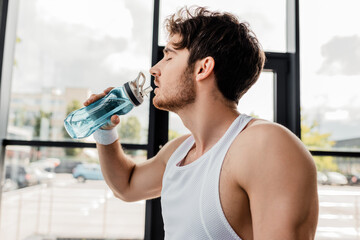 Fototapeta na wymiar side view of sportsman with closed eyes drinking water and holding sports bottle