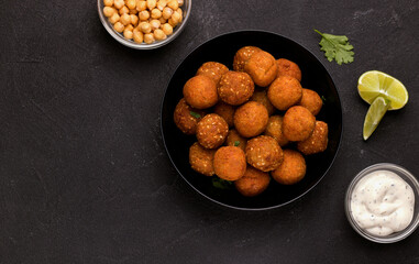 Falafel dish of chopped legumes, seasoned with spices on a black background with sauce and lime....