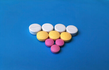 Assortative triangular pattern of med pills and capsules, isolated on blue, mixed pharmaceutical tablets.