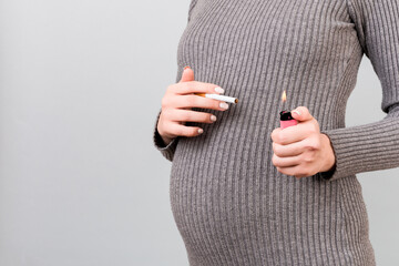 Close up of a cigarette and a lighter in pregnant woman's hands at gray background. Unhealthy habit during pregnancy. Smoking abuse