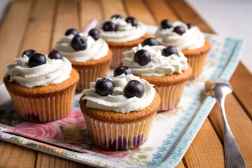 Homemade blueberry cup cake decorated with white cream and three blueberries lactose-free dessert, on natural wood
