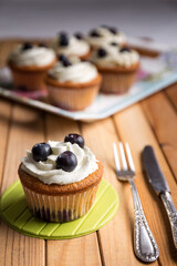 Homemade blueberry cup cake decorated with white cream and three blueberries lactose-free dessert, on natural wood
