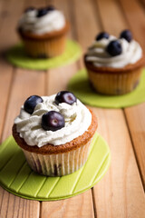 Homemade blueberry cup cake decorated with white cream and three blueberries lactose-free dessert, on natural wood
