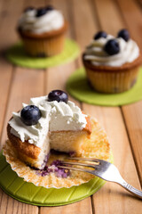 Homemade blueberry cup cake decorated with white cream and three blueberries lactose-free dessert, on natural wood
