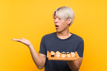 Young asian man with sushi over isolated yellow background holding copyspace imaginary on the palm