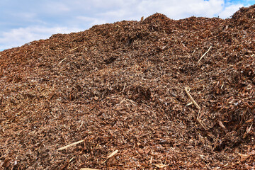 heap of tree bark removed from logs at a woodworking factory against sky