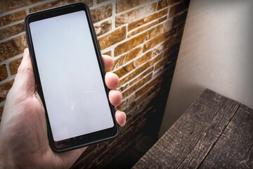 A smartphone with a white blank screen lies in a hand against the background of a home interior. Copy space