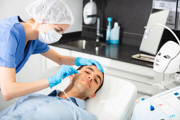 Fototapeta premium Young man patient receiving anti-aging injections carboxytherapy procedure in beautician office of aesthetic clinic