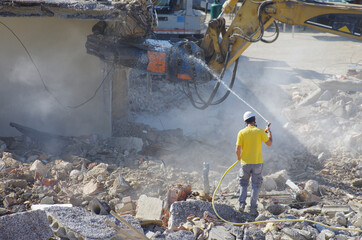 A worker uses the jet of water to lower the level of dust that forms during the demolition of a...