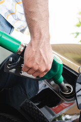 Cropped view of man holding fueling nozzle near open gas tank cover outdoors