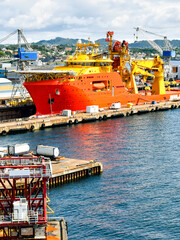 A large orange and yellow colored Offshore Construction Vessel (OCV) is in a dry dock of a shipyard and is being repaired