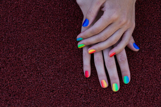 Hands with rainbow manicures on a dark brick background.