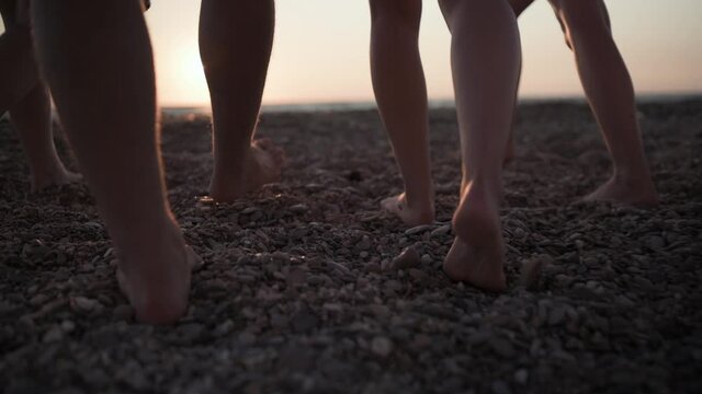 Group of the friends are walking across the beach at sunset party. Young men and women are walking by the sea. Close up view of poople feets
