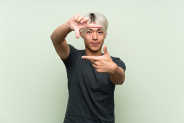 Young asian man over isolated green background focusing face. Framing symbol