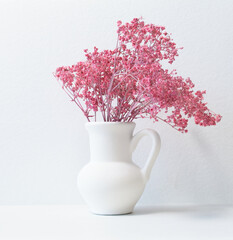 Small pink flowers in a white ceramic vase, on a white background. - 365012257