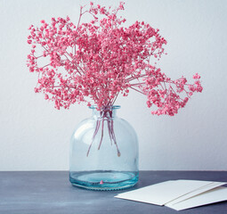 Still life. Small pink flowers in a glass bottle on a gray background and blank forms. Selective focus - 365012444