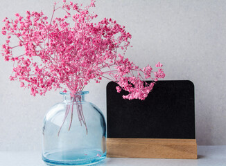 small pink flowers in a glass bottle and a black board for writing.copy space - 365012456