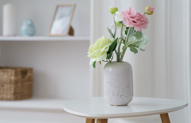 Pink and yellow roses in Modern white vase on white side table with copy space