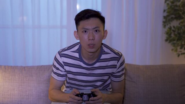 holiday leisure young man playing exciting racing game until midnight was nervous and just had a narrow win. asian man addicted to video games and yells in excitement for beating the level.