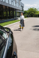 Selective focus of attractive businesswoman holding suitcase and walking to car on urban street