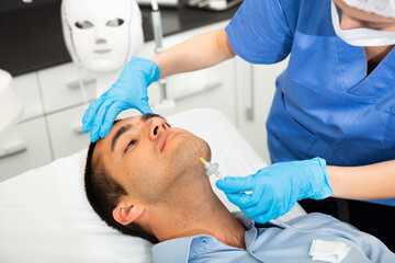 Young man patient receiving anti-aging injections carboxytherapy procedure in beautician office of aesthetic clinic